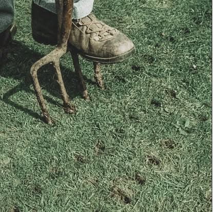 Gardener using a garden fork on green grass, highlighting outdoor planting activities.