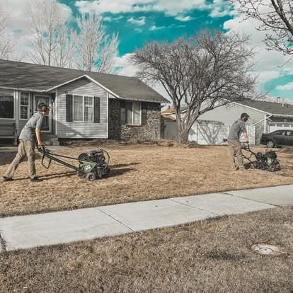 Lawn care professionals aerating a yard with machines on a sunny day.