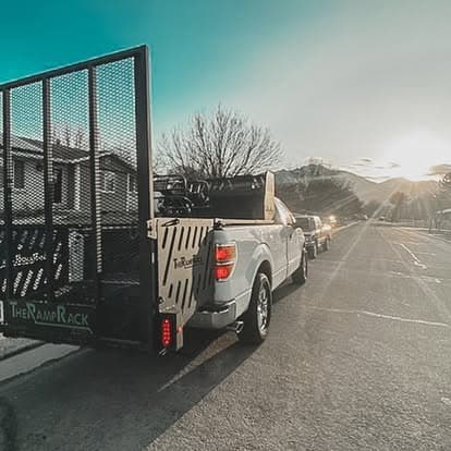 White truck with ramp rack parked on a street during sunset with mountains in the background.