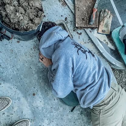 Person in gray hoodie resting on a chair amid construction tools and materials on the ground.