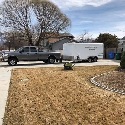 Lawn care truck and trailer parked near a dry lawn on a sunny day.